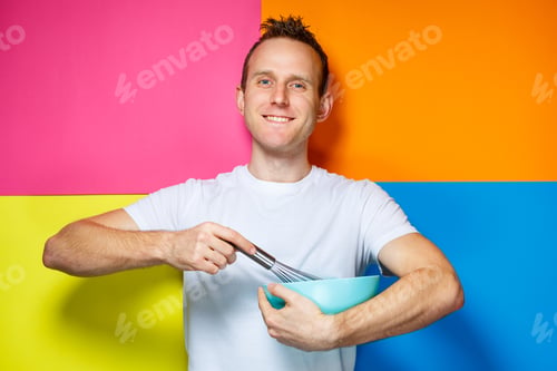 Preview: young guy man in a white T-shirt, colorful background, kitchen utensils, cook, emotions photo