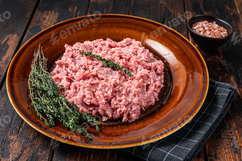 Preview: Ground chicken or turkey meat, raw Poultry on rustic plate with herbs. Dark background. Top View