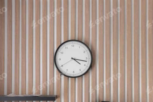Preview: A wall clock with a black frame and white face hangs prominently on a wooden striped wall, indicatin