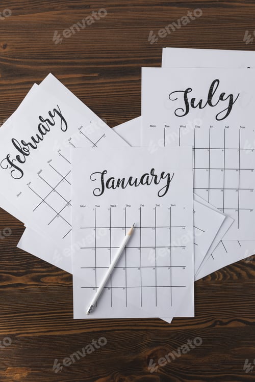 Preview: flat lay with arranged calendar papers and pencil on wooden tabletop