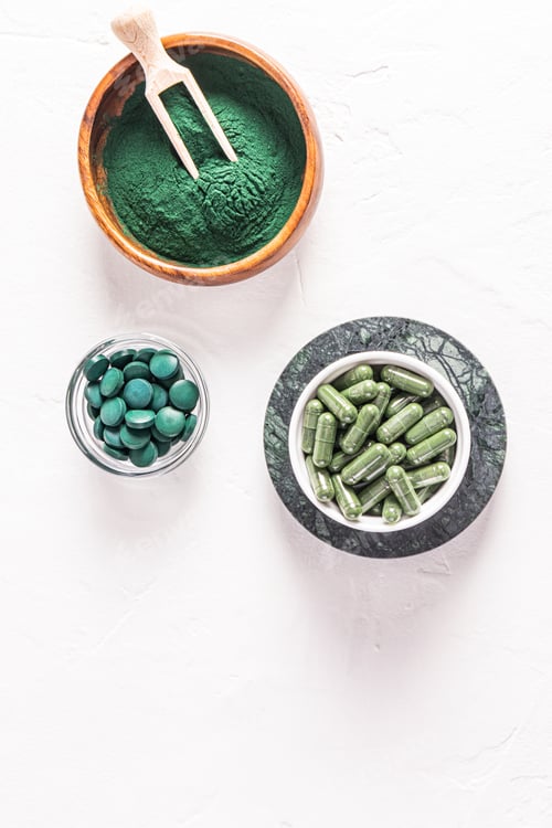 Preview: Green spirulina algae powder, capsules and tablets in jars on white embossed background.