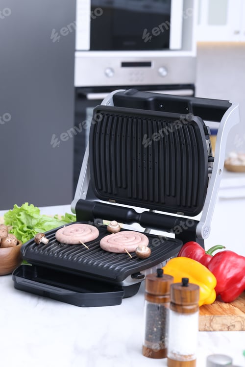Preview: Electric grill with homemade sausages, mushrooms, vegetables and spices on white table in kitchen
