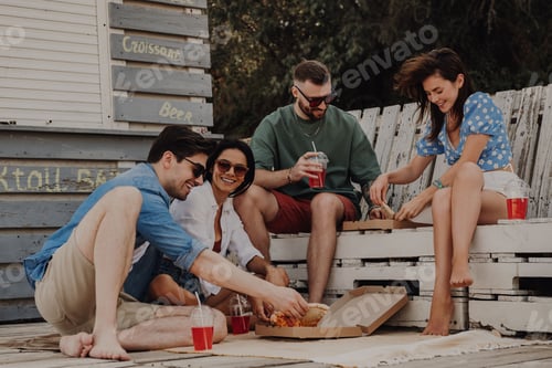 Preview: Group of happy friends enjoying food and drinks while relaxing near the beach cafe together