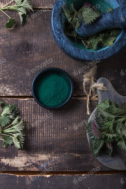Preview: nettle leaves on wooden table.Urtica dioica oil with spirulina powder, a healthy supplement