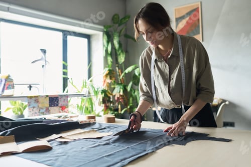 Preview: Young Adult Caucasian Woman Cutting Fabric While Working in Fashion Studio
