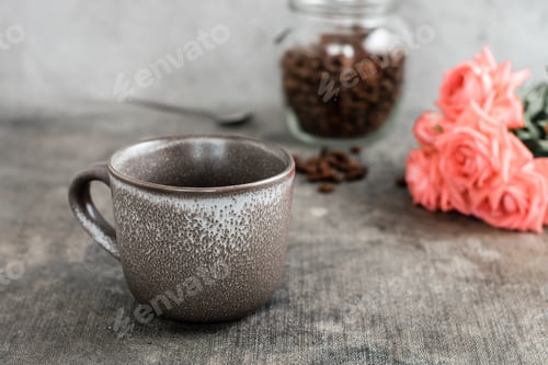 Preview: An empty ceramic coffee cup, a jar of coffee beans and a bouquet of roses on the table.