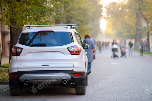 Preview: Car parked on a city street side on bright autumn day with blurred people walking on pedestrian zone