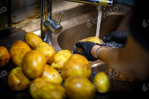 Preview: Hands with black plastic gloves washing potatoes under the faucet