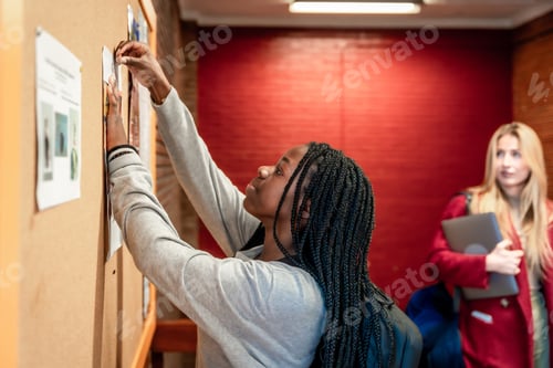 Preview: Young student putting up a notice on university bulletin board