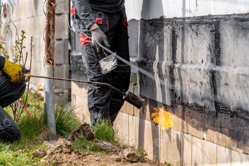 Preview: installation of protective waterproofing on the foundation and walls of the building. warmed by an