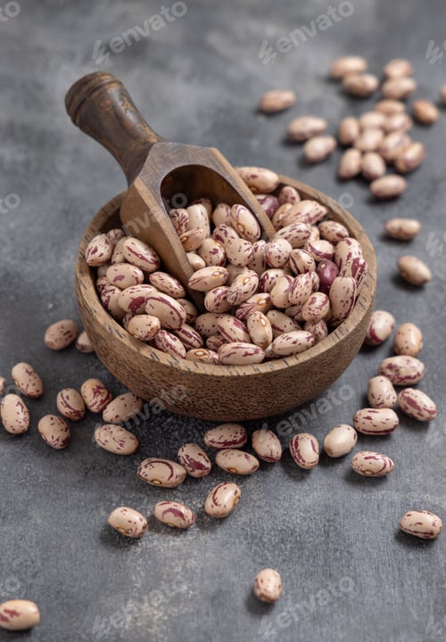 Preview: Wooden bowl full of dried pinto beans with scoop on gray closeup. Traditional Latin American legumes