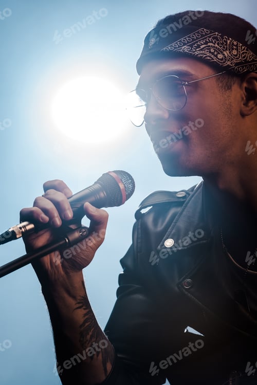 Preview: handsome male rock musician singing in microphone on stage with spotlight