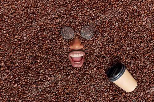 Preview: Emotional bearded man drowned in many coffee beans wears round glasses keeps mouth opened shows whit