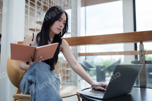 Preview: Freelancer working remotely using laptop and taking notes in notebook at cafe