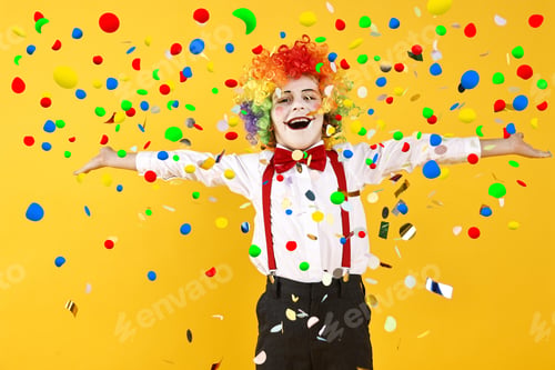 Preview: Happy boy dressed like clown under falling confetti on orange background. Party time