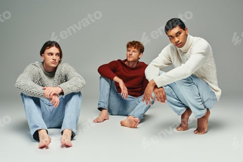 Preview: young african american man in sweater squatting with other two men sitting on floor, fashion concept