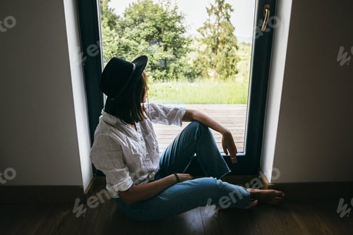 Preview: Fashionable hipster in casual cloth and hat relaxing on background of window with mountains hills