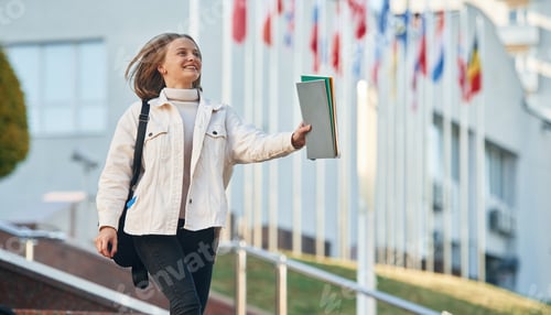 Preview: Against white university building. Young female student in casual clothes is outdoors