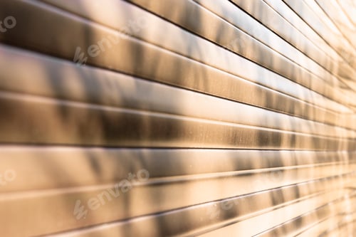 Preview: Brown wall of horizontal metal stripes with abstract tree shadow and sunlight.