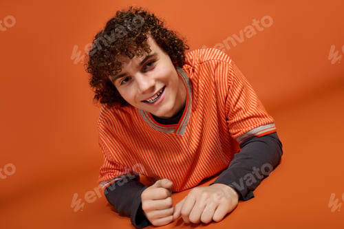 Preview: Curly teenage boy shows off casual style against vibrant orange backdrop