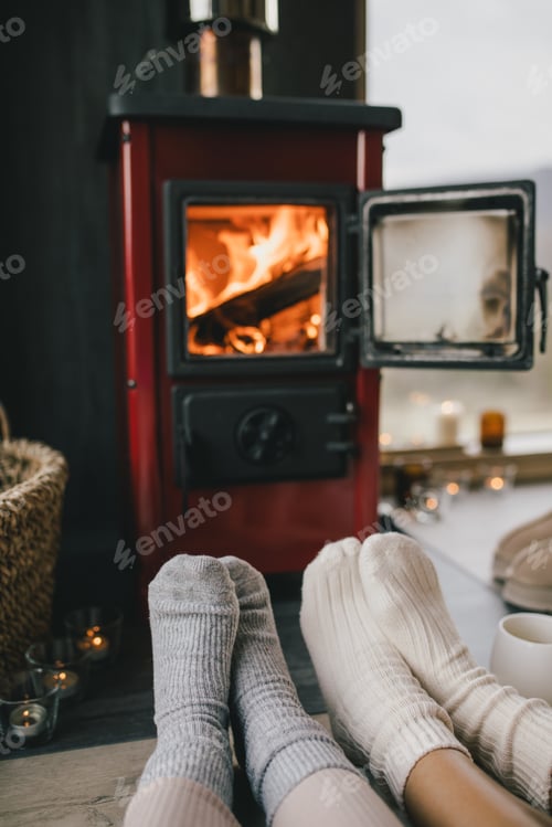 Preview: Two women sitting by the fireplace in knitted socks, drinking tea in cozy log cabin.