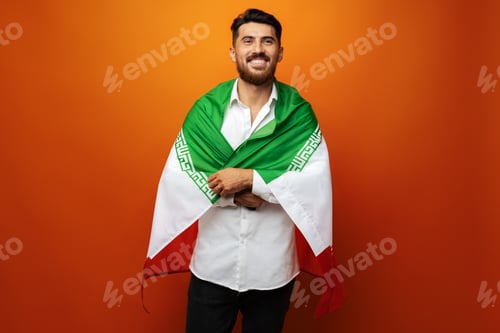 Preview: Portrait of a young casual man holding flag of Iran against orange background