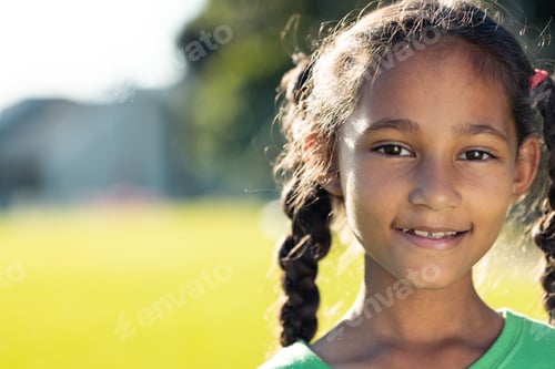 Preview: Portrait of biracial schoolgirl smiling in sunny elementary school sports field, copy space