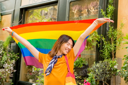 Preview: Happy LGBTQ+ youth with pride flag in street