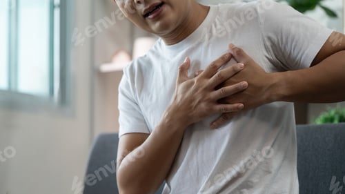 Preview: Chest Pain. Man holding chest in discomfort while seated at home.