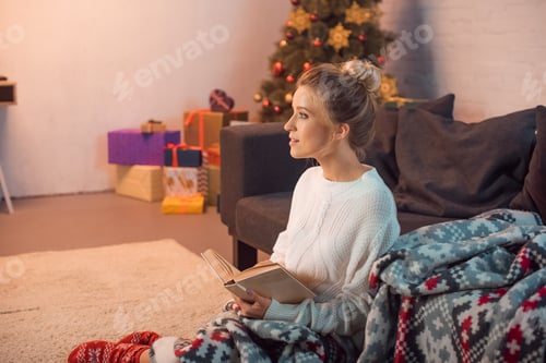 Preview: Charming girl smiling and reading book at home on Christmas eve
