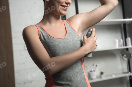 Preview: cropped view of smiling woman applying deodorant on underarm while standing near mirror at home