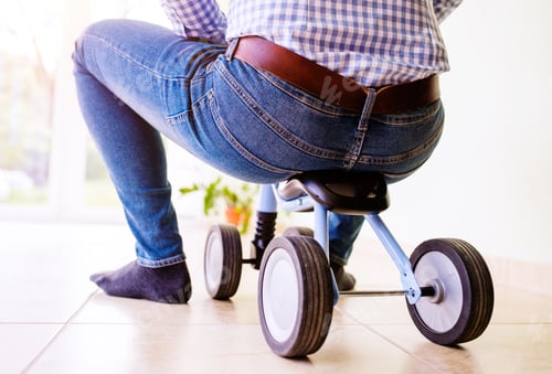 Preview: Hipster father riding a childrens bike indoors, sunny day