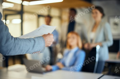 Preview: Focus on the male hand, reading a document to his employees in the background.