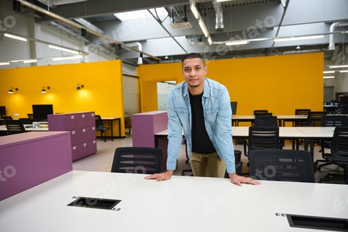 Preview: Joyful young man leaning on table while standing at office