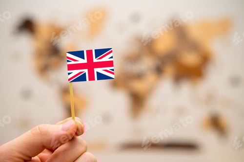 Preview: British flag in mans hand on the world map background.