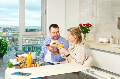 Preview: Young beautiful happy couple having breakfast together in kitchen at home. Lifestyle