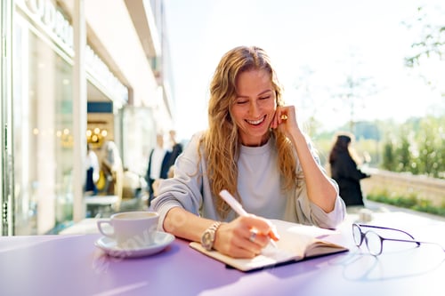 Preview: Casual woman sitting at table and taking notes in notebook .on the cafe terrace