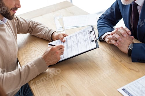 Preview: cropped view of man holding clipboard and signing agreement near car dealer