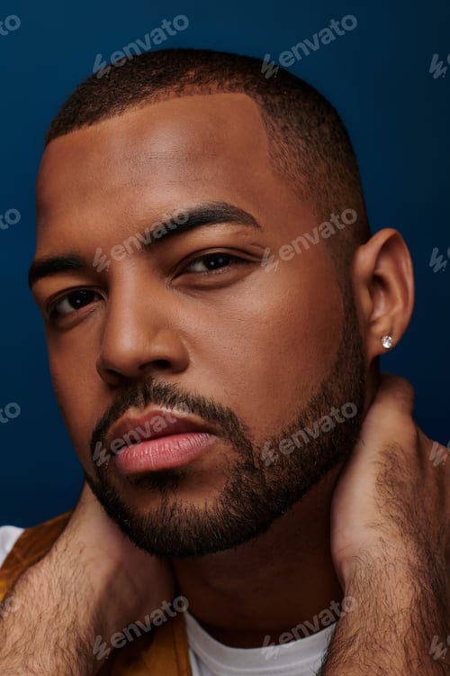 Preview: handsome man with diamond earring and beard looking at camera with hands on neck, fashion concept