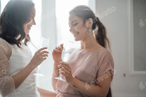 Preview: Two millennial candid lifestyle brunette girls in bridal outfits are having fun drinking champagne.