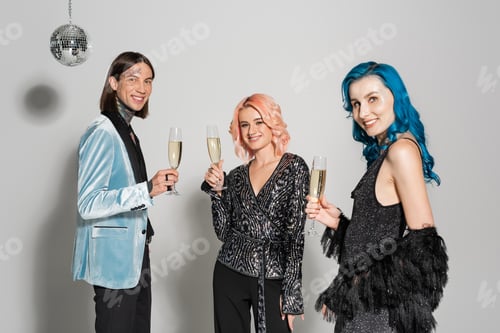 Preview: elegant queer people with glasses of champagne smiling at camera while celebrating christmas on