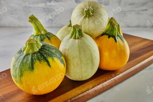 Preview: Round yellow and green zucchini on wooden board on gray background