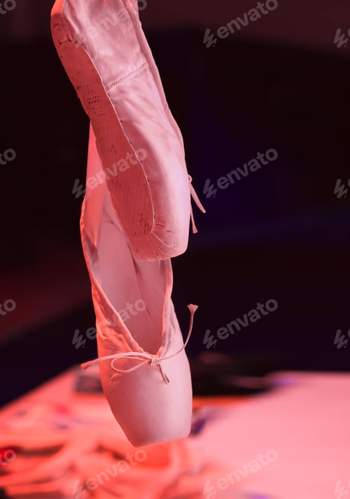 Preview: Pink ballet slippers hanging against dark background