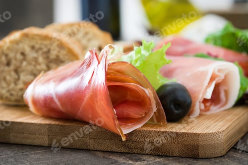Preview: Delicious iberian ham with black olives, bread and lettuce on a wooden cutting board