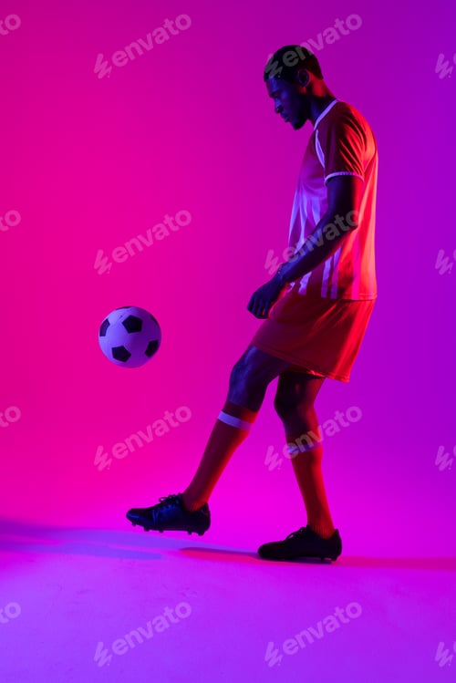 Preview: African american male soccer player with football over neon pink lighting