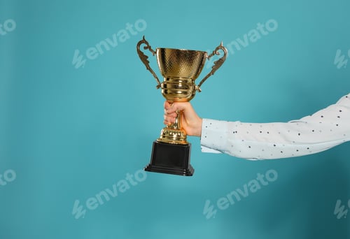 Preview: Young woman holding gold trophy cup on blue background, closeup