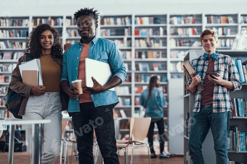 Preview: Enthusiastic Positive Students In Casual Clothes Standing In The Library With Cups Of Coffee In