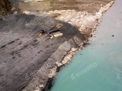 Preview: A cement factory tailings site with heavy machinery operating near a turquoise lake. Trucks and