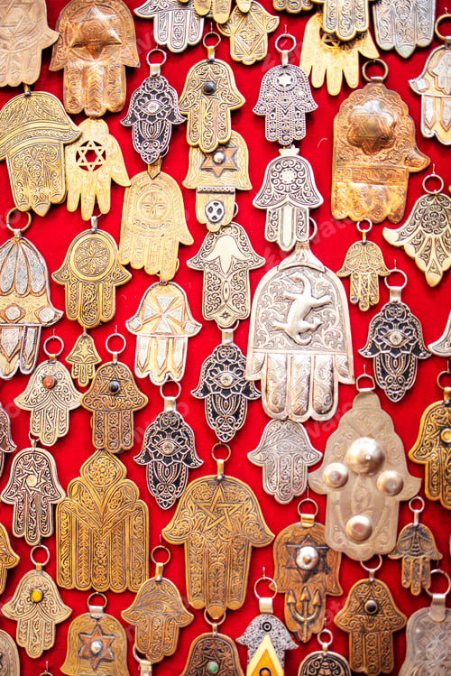 Preview: Intricate collection of metallic hand-shaped amulets displayed on vibrant red fabric