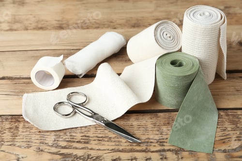 Preview: Medical bandage rolls, sticking plaster and scissors on wooden background